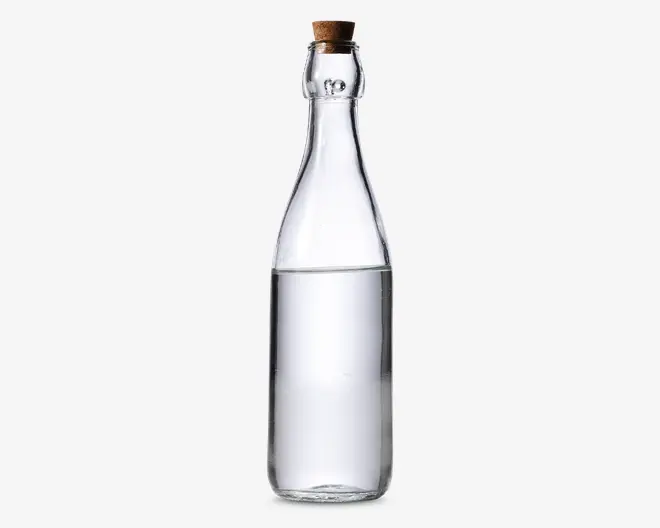 Klar glasflaske med en høj, smal hals og en prop af kork. Flasken er fyldt med en gennemsigtig væske op til cirka tre fjerdedele af dens højde. Glasset er glat og uden dekoration, hvilket giver flasken et minimalistisk og elegant udseende.