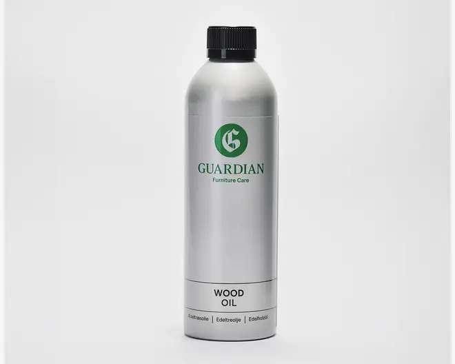 En høj, cylindrisk sølvfarvet metalflaske med sort skruelåg. Flasken har et grønt logo og mærket 'Guardian Furniture Care' trykt på forsiden. Nederst på etiketten står der tydeligt 'Wood Oil' og yderligere tekst på flere sprog. Designet er stilrent og moderne med et minimalistisk udtryk.