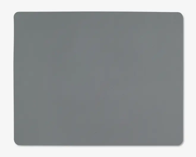 Et rektangulært underlag med afrundede hjørner og en glat, ensfarvet grå overflade. Kanterne er let hævede, og materialet ser blødt og fleksibelt ud, velegnet til brug på et skrivebord eller bord.