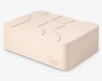 Rektangulær opbevaringsboks i cremefarvet med en glat, mat overflade. Låget har et hævet, abstrakt geometrisk mønster, der giver tekstur og visuel interesse. Ordet 'Tea' er trykt med elegant, lysegylden skrift på forsiden. Boksen har afrundede hjørner og et moderne, minimalistisk design.