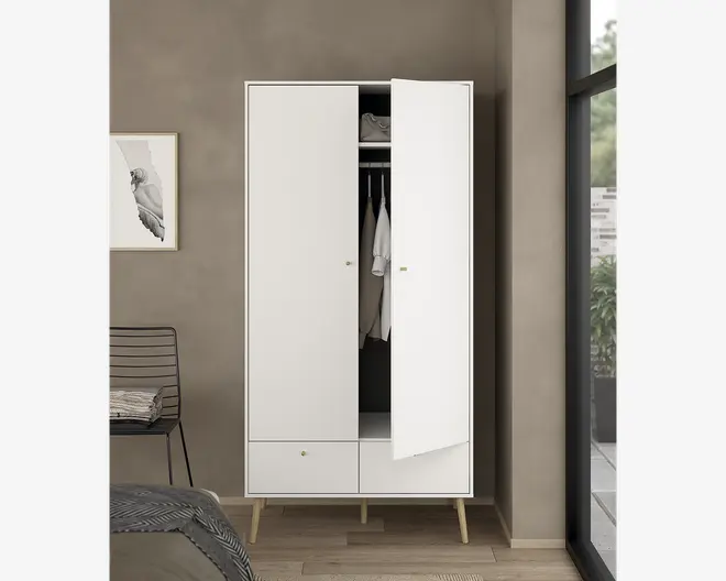 Høj, fritstående garderobe med minimalistisk design, to hvide låger hvor den ene er let åben og viser en bøjlestang med tøj samt en øverste hylde til opbevaring. Garderoben har to rummelige skuffer nederst og står på fire skrå ben i lyst træ, hvilket giver et moderne og let udtryk.