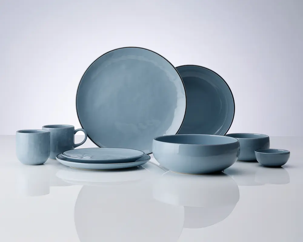 Et sæt matchende keramikservice i en blød mat blå farve, bestående af to store middagstallerkener, to mindre sidetallerkener, to skåle i forskellige størrelser, to krus med hank og to små dip-skåle. Delene har en glat, let afrundet form og et diskret, håndglaseret udtryk, som giver hvert element et unikt, håndlavet præg.