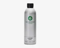 En høj, cylindrisk sølvfarvet flaske med sort skruelåg. Etiket med grønt, cirkulært logo med et 'G' og teksten 'GUARDIAN Furniture Care' i grøn skrift. Under logoet står der 'LEATHER SOAP' med store sorte bogstaver, og nederst er der oversættelser til flere sprog. Flasken har et stilrent, moderne design og ser ud til at være lavet af metal eller metallisk plast.