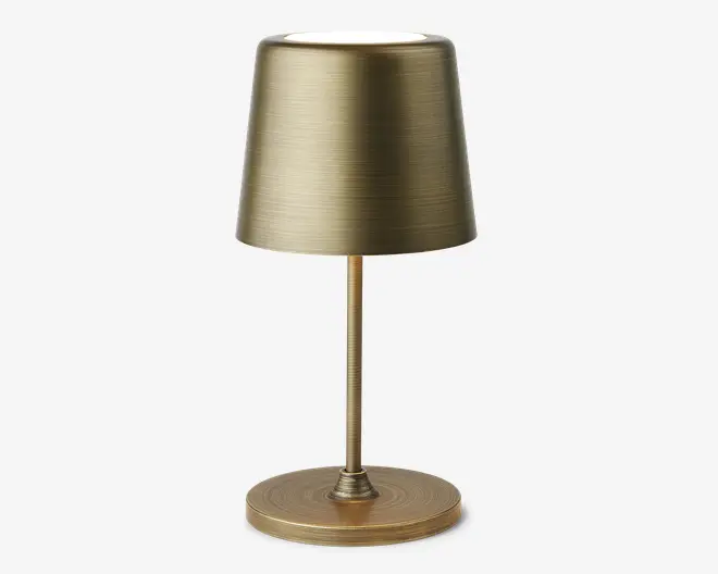 En moderne bordlampe med børstet messingfinish. Lampen har en cylindrisk fod, en slank stang og en let konisk, tromleformet skærm. Den metalliske overflade har en diskret horisontal tekstur, hvilket giver lampen et sofistikeret og moderne udtryk.