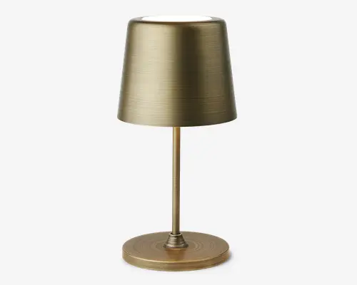 En moderne bordlampe med børstet messingfinish. Lampen har en cylindrisk fod, en slank stang og en let konisk, tromleformet skærm. Den metalliske overflade har en diskret horisontal tekstur, hvilket giver lampen et sofistikeret og moderne udtryk.