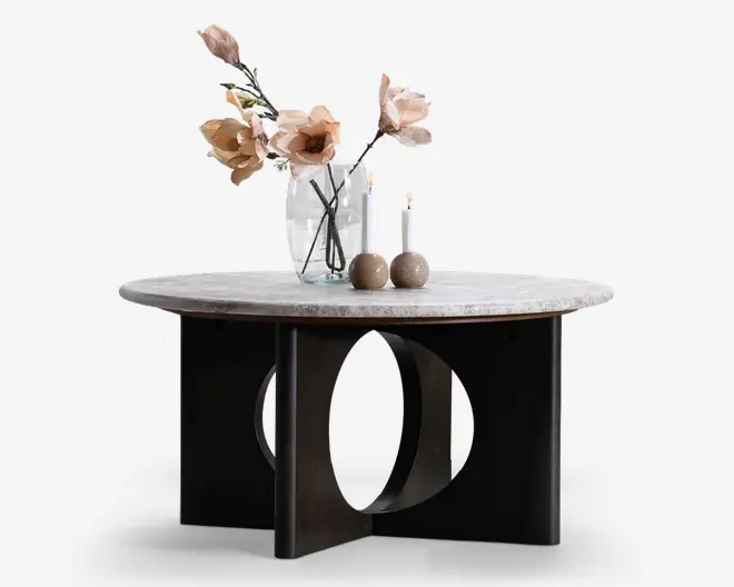 Rundt sofabord med lys stenlignende bordplade og en skulpturel sort base med store cirkulære udskæringer og lodrette paneler, som giver et moderne, minimalistisk udtryk.