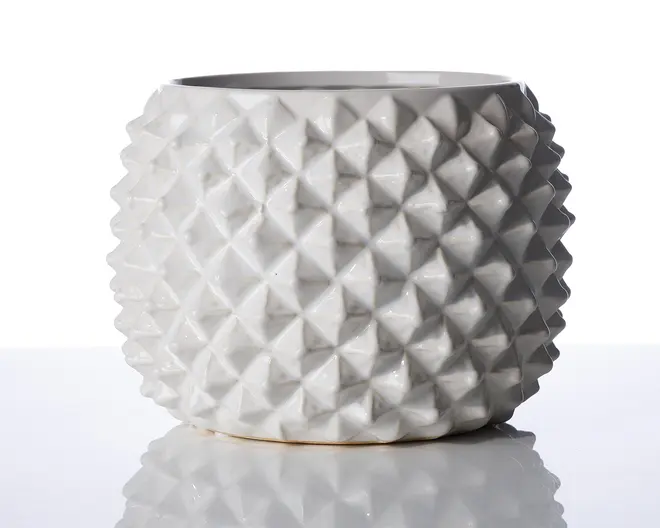 En rund, hvid keramisk beholder med en markant geometrisk tekstur, der består af hævede diamantformede knopper over hele ydersiden. Overfladen er blank, hvilket giver et moderne og stilfuldt udtryk. Åbningen foroven er bred, og det samlede design er både dekorativt og funktionelt.