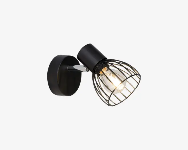 Væghængt lampe med mat sort finish, rund base og justerbar arm. Lampens hoved har et dekorativt åbent metalgitter, som gør pæren synlig og giver et industrielt udtryk. Pæren udsender et varmt lys, og lampen egner sig til retningsbestemt belysning.