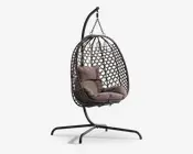 Hængende æggeformet stol med flettet rattanramme, ophængt fra et robust sort metalstativ. Stolen har bløde, taupefarvede sæde- og ryghynder for ekstra komfort. Den åbne gitterstruktur i rammen giver god luftcirkulation og et moderne udtryk. Basen er bred og stabil, hvilket sikrer sikker placering både indendørs og udendørs.