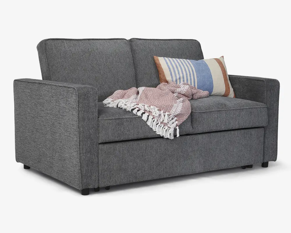 En moderne 2-personers sofa betrukket med mørkegråt stof, med rene, lige linjer og firkantede armlæn. Sædehynderne er faste, og ryghynderne er let skrånende for komfort. Over den ene side ligger et tekstureret, lyserødt og hvidt plaid med frynser, og der er en dekorativ pude med stribet mønster i blå, hvid og tan nuancer, som tilføjer farve og hygge.