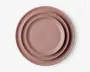 Sæt med tre runde tallerkener i forskellige størrelser, alle i en mat soppefarvet rosa. Tallerkenerne har et enkelt, minimalistisk design med glat overflade og let hævede kanter. De er stablet pænt fra den mindste til den største |.