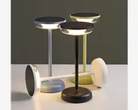 Tre moderne bordlamper med cirkulære, flade toppe og slanke cylindriske stænger i sort, hvid og lysegrøn. Lampetoppe har integreret LED-belysning langs kanten, hvilket giver et blødt, stemningsfuldt lys. Basen er rund og solid, og matcher stængernes farve. Én lampe ligger vandret, hvilket fremhæver dens lette og bærbare design. Lamperne har et minimalistisk, moderne udtryk, der passer til forskellige indretninger.