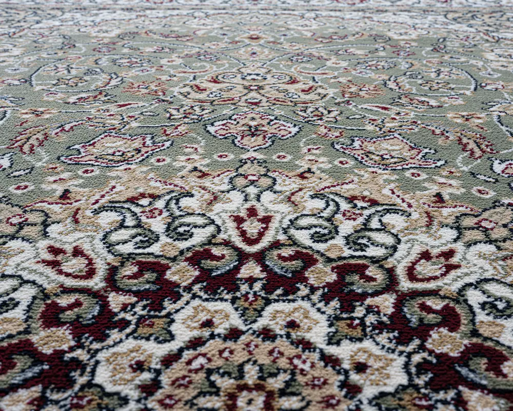 Nærbillede af en overflade med indviklede blomster- og geometriske mønstre i grønne, cremefarvede, bordeauxrøde og beige nuancer. Teksturen ser blød og fyldig ud, med detaljerede konturer og symmetriske designs, der giver et klassisk og elegant udtryk.