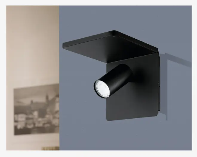 Et moderne, minimalistisk vægmonteret armatur med mat sort finish. Designet har en rektangulær bagplade og en matchende vandret hylde øverst, med en cylindrisk, justerbar spotlampe, der stikker ud. Spotlampen kan rettes, så lyset fokuseres, hvor det er nødvendigt, hvilket gør den velegnet til læsning eller accentbelysning. Armaturet har rene linjer og et nutidigt udtryk, ideelt til moderne indretning.