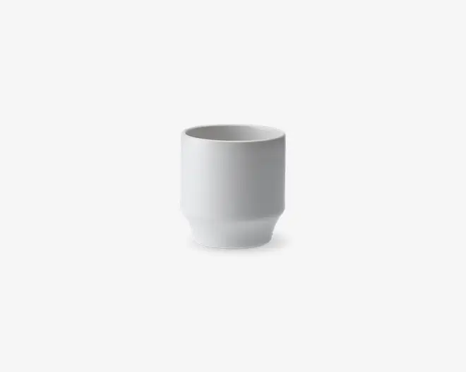 En lille, cylindrisk hvid keramikkop med en glat, mat overflade. Koppen har lige sider og en lidt tykkere bund, hvilket giver et moderne og minimalistisk udtryk. Der er ingen hank eller dekorative elementer.