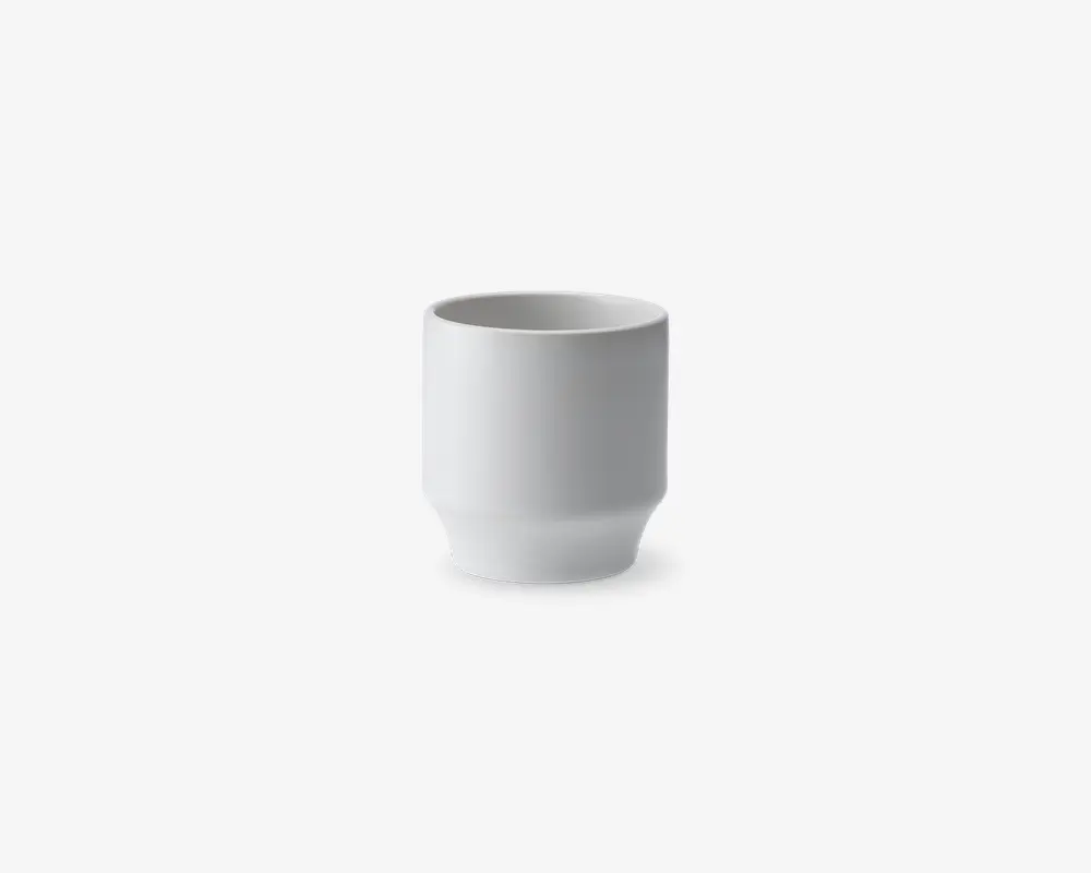 En lille, cylindrisk hvid keramikkop med en glat, mat overflade. Koppen har lige sider og en lidt tykkere bund, hvilket giver et moderne og minimalistisk udtryk. Der er ingen hank eller dekorative elementer.
