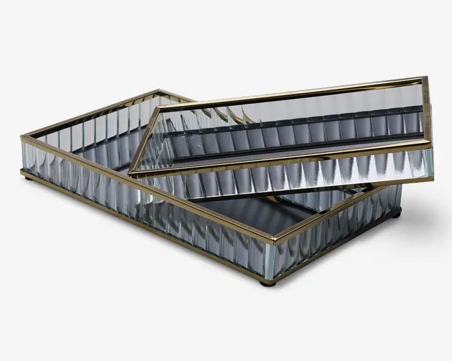 Rektangulær bakke med spejloverflader og lodrette, riflede glassider, indrammet af en slank guldfarvet metalramme. Bakken har et moderne, elegant design og vises med en mindre matchende bakke placeret indeni.