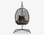Hængende æggeformet stol med flettet rattanramme, understøttet af et robust metalstativ. Stolen har bløde, mørkebrune puder, herunder en siddepude, to sidepuder og en rygpude for ekstra komfort. Den åbne fletning giver god luftcirkulation og et moderne udseende, hvilket gør den velegnet til både indendørs og udendørs brug.