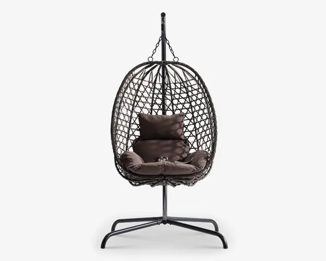 Hængende æggeformet stol med flettet rattanramme, understøttet af et robust metalstativ. Stolen har bløde, mørkebrune puder, herunder en siddepude, to sidepuder og en rygpude for ekstra komfort. Den åbne fletning giver god luftcirkulation og et moderne udseende, hvilket gør den velegnet til både indendørs og udendørs brug.