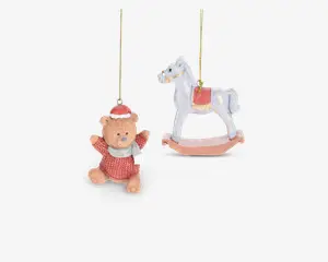 To hængende dekorationer: den ene er en bamse iført rød sweater, hvidt tørklæde og rød nissehue, med et venligt udtryk og udstrakte arme; den anden er en hvid gyngehest med rød saddel og gyldne detaljer, begge ophængt i gyldne snore.