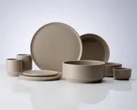 Et sæt mat beige keramikservice med minimalistisk design. Sættet indeholder store og små tallerkener, skåle i forskellige størrelser og kopper. Alle dele har glatte overflader, lige kanter og en ensartet farve, hvilket giver et moderne og elegant udtryk.
