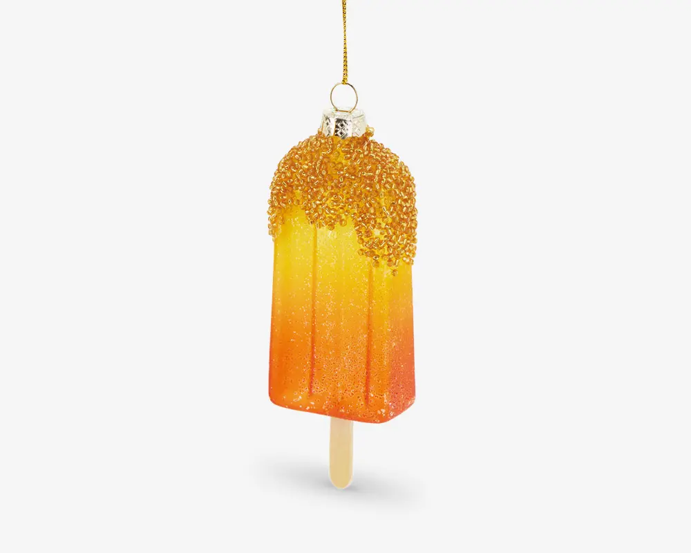 En dekorativ ornament formet som en ispind, med en farveovergang fra orange til gul og et glitrende finish. Toppen af ornamentet er dækket af gyldne perler, der ligner krymmel, og det hænger i en gylden snor. Ornamentet har en realistisk træpind i bunden.