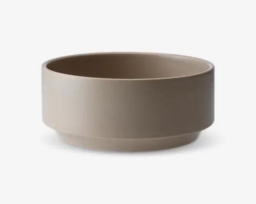 En rund skål med mat finish i en afdæmpet taupe farve. Skålen har lige sider, en flad bund med en diskret forhøjet kant og et minimalistisk, moderne design uden synlige mønstre eller dekorationer.