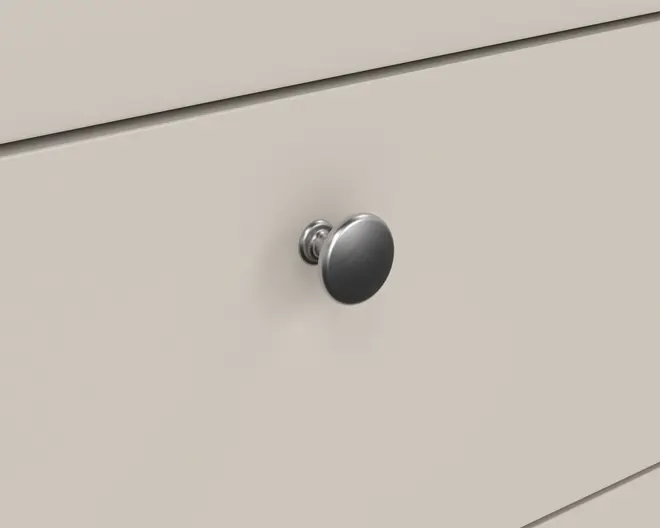 Nærbillede af en skuffefront med en rund, metalgreb. Grebet har en glat, børstet overflade og et enkelt, klassisk design med en let hævet base. Skuffens overflade er flad og malet i en lys beige eller offwhite farve, hvilket giver et rent og moderne udtryk.