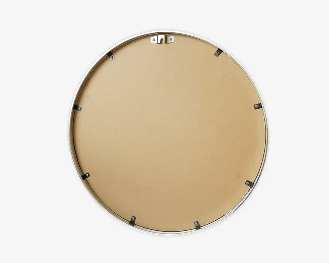 Billedet viser bagsiden af en rund genstand med en glat, lysebrun overflade, sandsynligvis lavet af MDF eller lignende materiale. Der er en sølvfarvet metalramme rundt i kanten og flere sorte metalclips jævnt fordelt for at fastgøre bagbeklædningen. Øverst er der et metalophæng til vægmontering.