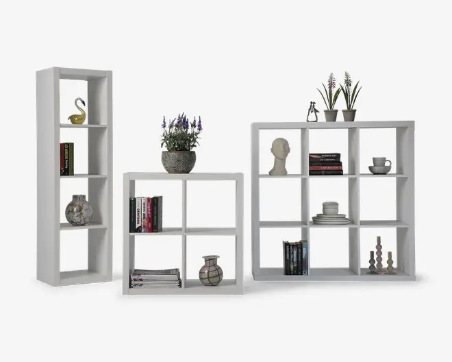 Tre modulære reolenheder i et moderne, minimalistisk design med hvid finish. Enhederne varierer i størrelse: én er høj og smal med fire kvadratiske rum, en anden er mellemstor med fire kvadratiske rum i et 2x2 gitter, og den største har ni kvadratiske rum i et 3x3 gitter. Hylderne er dekoreret med pyntegenstande som bøger, potteplanter, en skulpturhoved, vaser og skåle, hvilket viser deres alsidighed til opbevaring og udstilling.