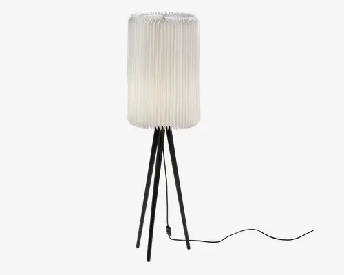Høj gulvlampe med en cylindrisk, plisseret hvid lampeskærm, der giver et blødt lys. Lampen står på en unik fod bestående af flere slanke sorte metalben, der spreder sig udad for stabilitet. En sort ledning er synlig og går ud fra lampens fod.