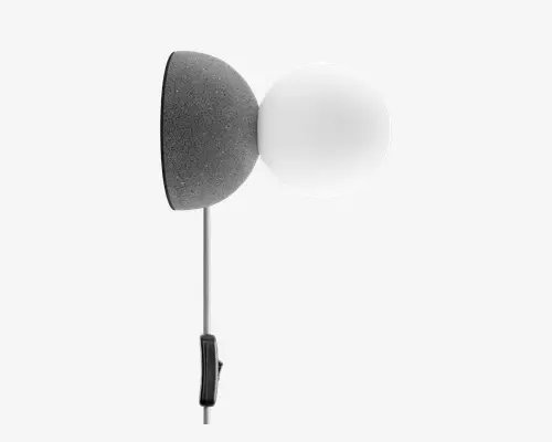 Væghængt lampe med en rund, tekstureret mørkegrå base og en glat, hvid matteret glaskuppel som skærm. Lampen har en slank, lodret metalstang med en lille sort kontakt eller håndtag nederst for nem betjening. Designet er moderne og minimalistisk, velegnet til nutidige indretninger.