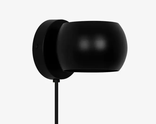 Væghængt armatur i mat sort med en rund, kuppelformet skærm. Designet er minimalistisk og moderne med en glat overflade uden synlige dekorationer. Armaturet har en ledning, der går ud fra bunden, og skærmen leder lyset nedad. Velegnet til moderne indretning.