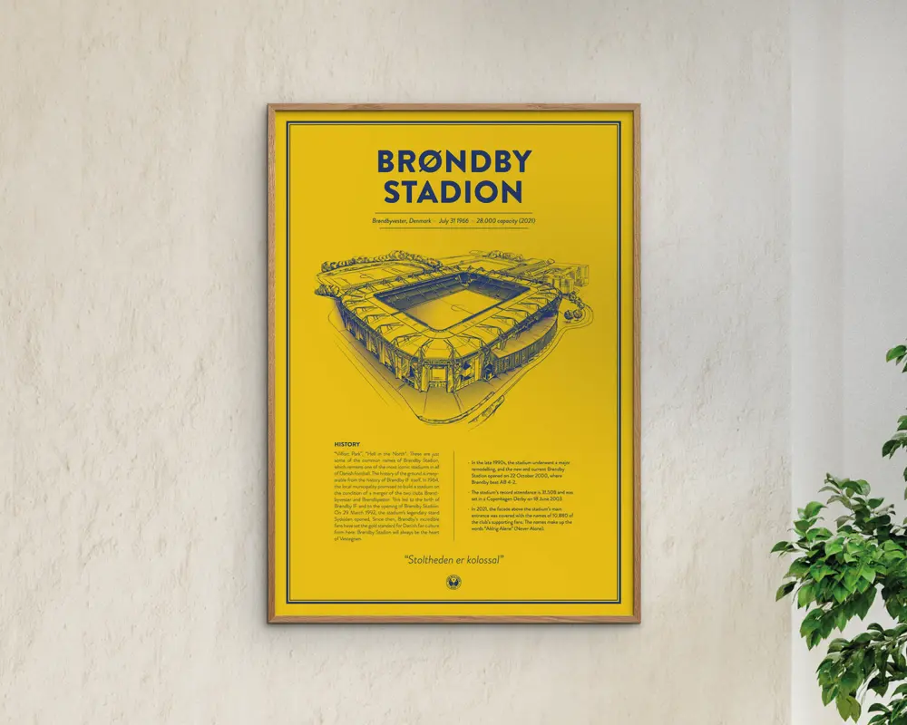 En indrammet plakat med en klar gul baggrund og en tynd sort kant. Plakaten viser en detaljeret stregtegning af et stadion i blå blæk, placeret centralt. Over illustrationen står der med fed blå skrift 'BRØNDBY STADION.' Under tegningen er der tekstafsnit i mindre blå skrift, herunder en historiedel og et citat. Designet er minimalistisk og moderne med en stærk kontrast mellem den gule baggrund og de blå elementer.