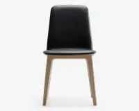 Stol med glat, sort, høj ryg og sæde, der har et minimalistisk design. Benene er lavet af lyst træ og har en let vinklet form, hvilket giver et moderne og enkelt udtryk. Sædet og ryglænet ser ud til at være polstret med et læderlignende materiale.