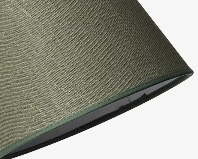 Nærbillede af en lampeskærm med olivengrønt tekstil på ydersiden og en glat, lidt mørkere grøn kant langs bunden. Indersiden af skærmen ser ud til at være foret med et lyst materiale.