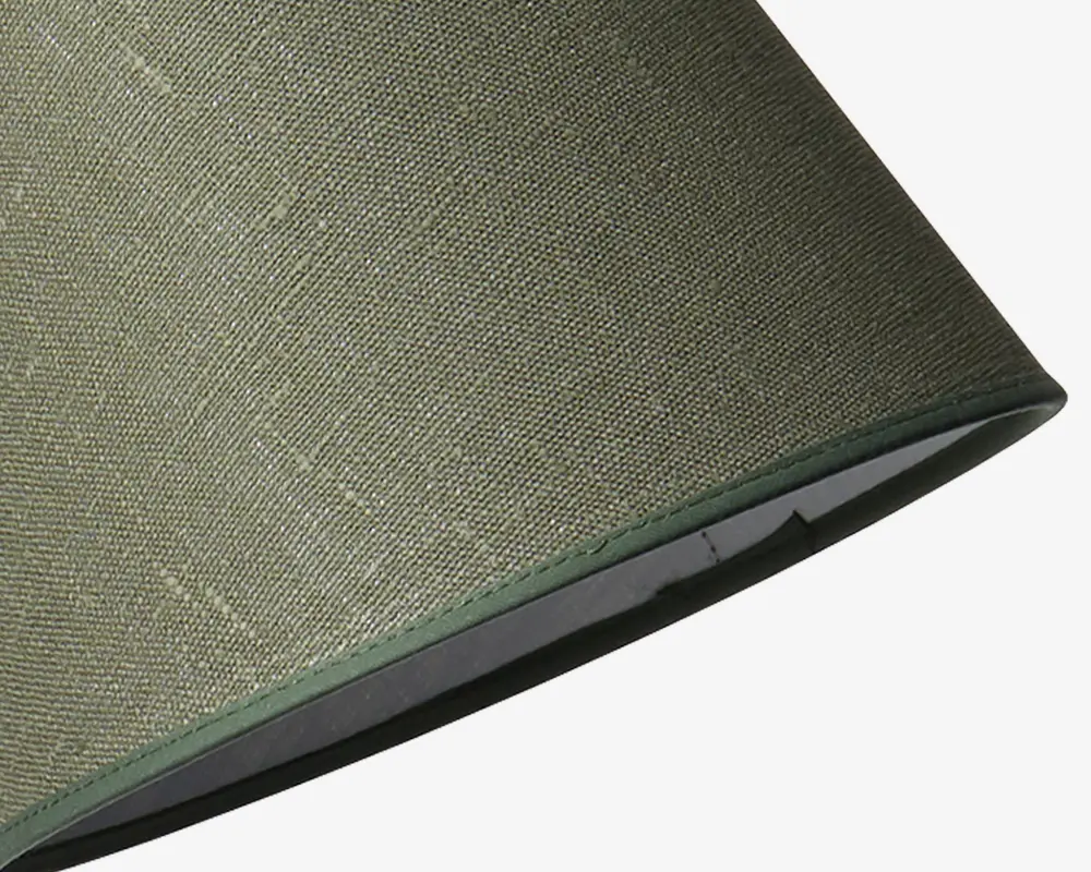 Nærbillede af en lampeskærm med olivengrønt tekstil på ydersiden og en glat, lidt mørkere grøn kant langs bunden. Indersiden af skærmen ser ud til at være foret med et lyst materiale.