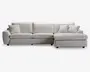 En moderne, L-formet sofa med chaiselong på højre side. Betrækket er i et lyst beige stof med en blød, tekstureret overflade. Sofaen har tre store sædehynder, tre matchende ryghynder og tre pyntepuder for ekstra komfort. Armlænene er brede og let afrundede, hvilket giver møblet et moderne og indbydende udtryk.