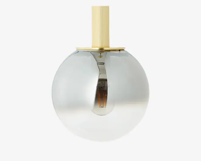 En moderne pendellampe med en kugleformet glasskærm, der har en diskret farveovergang fra klar i bunden til røgfarvet i toppen. Lampen har en messing- eller guldfarvet metalstang og top, hvilket giver et stilrent og elegant udtryk. Pæren er synlig inde i lampen, hvilket understreger det moderne design.