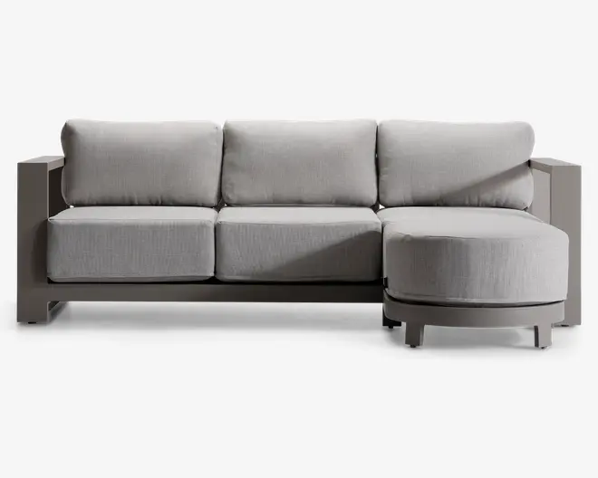 Moderne sofa med sektion og chaiselong på højre side. Sofaen har tykke, lysegrå hynder på både sæde og ryg, hvilket giver god komfort. Stellet er robust og kantet med en mat finish, og chaiselongen har en afrundet front for ekstra stil. Armlænene er brede og flade, hvilket gør dem velegnede til at hvile ting på. Designet er minimalistisk og moderne.