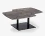 Rektangulært bord med en unik, asymmetrisk bordplade i marmor med naturlige grå og hvide årer. Bordpladen har et moderne, geometrisk udskæringsdesign på den ene side, hvilket giver et spændende visuelt udtryk. Bordet understøttes af to sorte metalben, der er fastgjort til en solid, firkantet sort metalfod for stabilitet og et moderne udseende.
