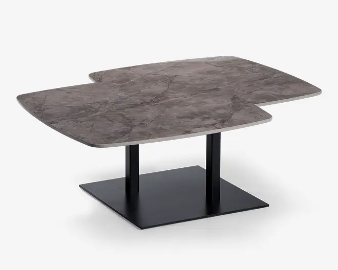 Rektangulært bord med en unik, asymmetrisk bordplade i marmor med naturlige grå og hvide årer. Bordpladen har et moderne, geometrisk udskæringsdesign på den ene side, hvilket giver et spændende visuelt udtryk. Bordet understøttes af to sorte metalben, der er fastgjort til en solid, firkantet sort metalfod for stabilitet og et moderne udseende.