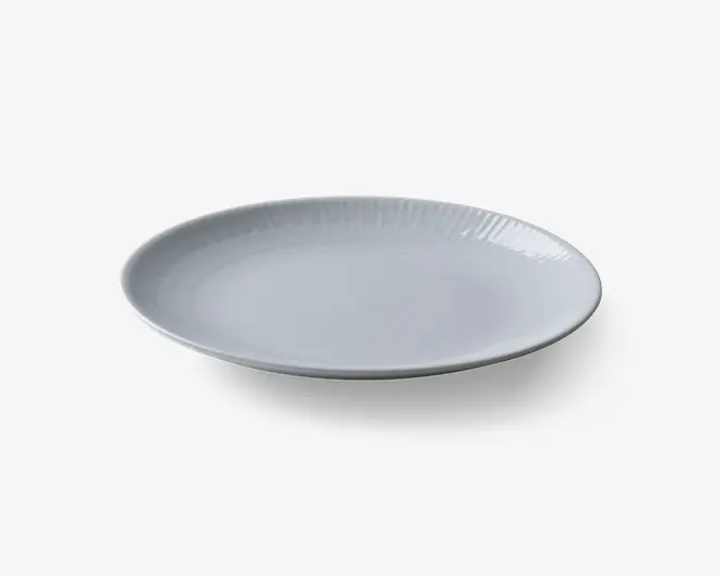 Rund, hvid tallerken med en glat, blank overflade og et diskret, hævet mønster langs kanten. Tallerkenen har en let buet kant, hvilket giver den et moderne og elegant udseende.