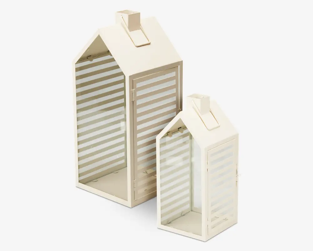 To dekorative lanterner med husformet design, fremstillet af cremefarvet metal og klare glaspaneler med vandrette frostede striber. Hver lanterne har et saddeltag og en rektangulær bund samt et lille håndtag på toppen til nem transport eller ophængning. Lanternerne vises i to forskellige størrelser og er velegnede til stearinlys eller LED-lys.