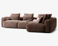 En stor, moderne hjørnesofa med chaiselong til højre, betrukket med et tekstureret brunt stof. Sofaen har brede, dybe sæder og tykke, afrundede armlæn for ekstra komfort. Den leveres med seks matchende ryghynder og to mindre pyntepuder, som giver god støtte. Et magasin og et let tæppe ligger afslappet på chaiselongen, hvilket skaber en hyggelig og indbydende stemning.