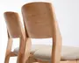Nærbillede af to stole med glatte, lyse trærammer og let buede ryglæn. Sæderne er polstret med et blødt, lysebeige stof, der giver en behagelig siddekomfort. Designet fremhæver rene linjer og et moderne, minimalistisk udtryk.