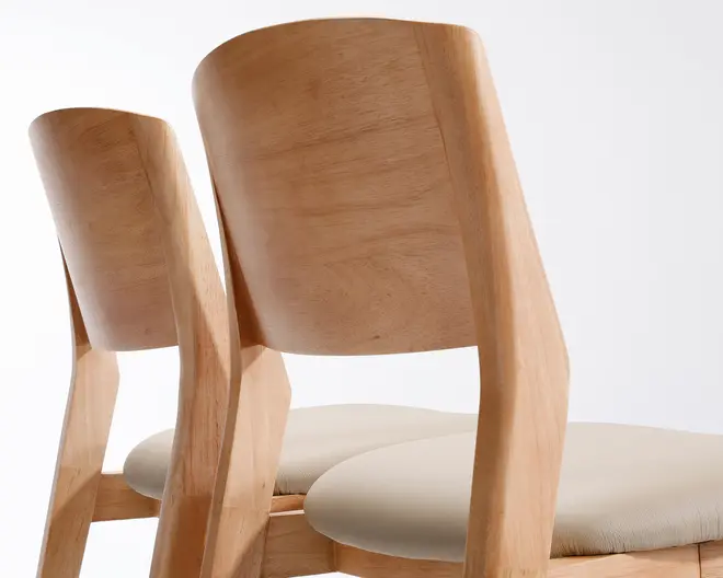 Nærbillede af to stole med glatte, lyse trærammer og let buede ryglæn. Sæderne er polstret med et blødt, lysebeige stof, der giver en behagelig siddekomfort. Designet fremhæver rene linjer og et moderne, minimalistisk udtryk.