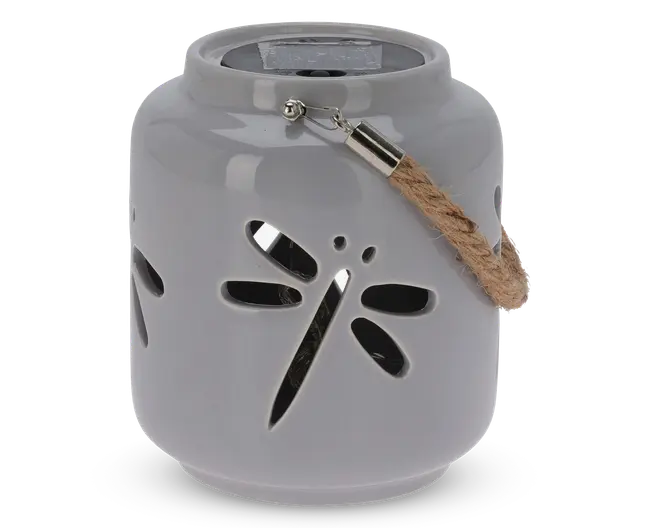 En rund, blank keramiklanterne med udskåret guldsmed-design på siden. Lanternen er lysegrå og har et robust rebhåndtag, der er fastgjort med metalbeslag. Øverst på lanternen sidder et solpanel, hvilket viser, at den er solcelledrevet til belysning.