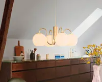 Et moderne loftophængt lampearmatur med en guldfarvet metalramme og fem matterede glaskupler arrangeret i en cirkel. Lampen hænger i en enkelt ledning og giver et blødt, diffust lys. Designet er stilrent og nutidigt, velegnet til spise- eller opholdsrum.