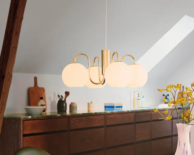 Et moderne loftophængt lampearmatur med en guldfarvet metalramme og fem matterede glaskupler arrangeret i en cirkel. Lampen hænger i en enkelt ledning og giver et blødt, diffust lys. Designet er stilrent og nutidigt, velegnet til spise- eller opholdsrum.